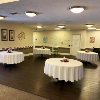 An indoor event space featuring round tables with white tablecloths and simple decor.