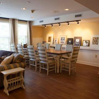 A spacious conference room featuring a long wooden table surrounded by chairs, couches for seating, and artwork adorning the walls.