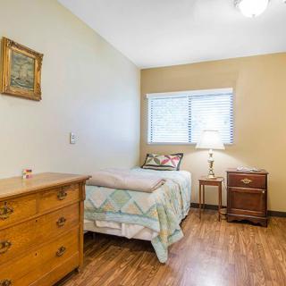 A cozy bedroom with a single bed, wooden floor, dresser, nightstand, and a lamp by the window.