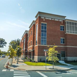 A red brick building with a clear blue sky in the background, surrounded by trees and a crosswalk in front.
