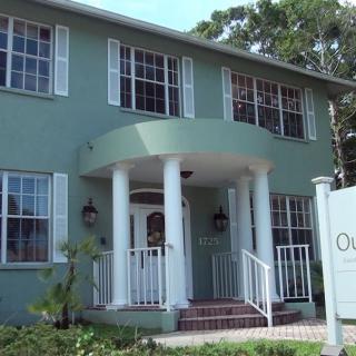 A green two-story building with a columned entrance and large windows.