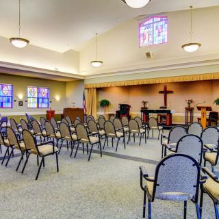 An interior view of a church chapel with rows of chairs and stained glass windows.