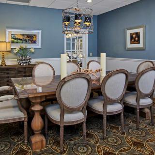 A beautifully decorated dining room featuring a long wooden table surrounded by elegant chairs, with a chandelier above and artwork on the walls.