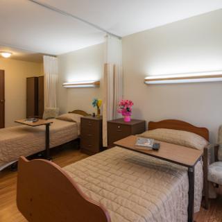 A spacious hospital room featuring two beds with bedside tables and soft lighting.