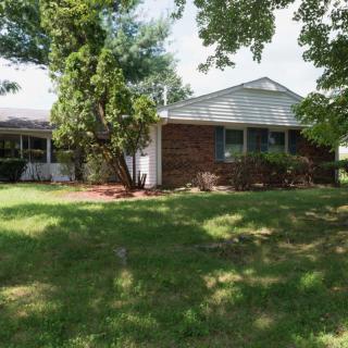 Suburban house with a brick facade surrounded by trees and a well-kept lawn.