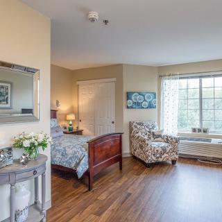 A cozy bedroom with a wooden bed, armchair, and large window.