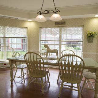 A well-lit dining room featuring a spacious table and wooden chairs with large windows allowing natural light to flood the space.