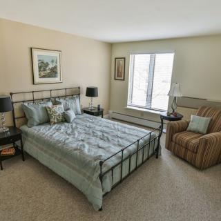 A cozy bedroom featuring a metal-framed bed, an armchair, and a window allowing natural light.