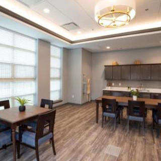 A modern dining room with a kitchen area, featuring wood flooring and elegant lighting.