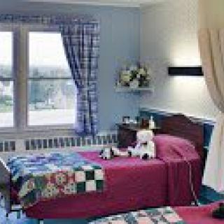A cozy room with a bed, teddy bear, and quilted blanket near a window.