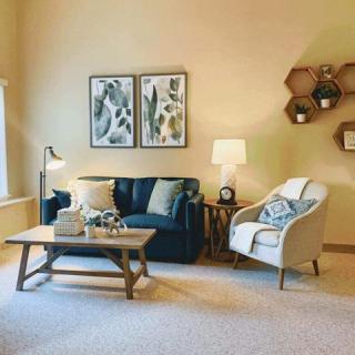 A cozy living room with a navy sofa, armchair, wooden coffee table, wall art, and warm lighting.