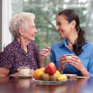 An elderly woman and a younger woman enjoying coffee and conversation at home.