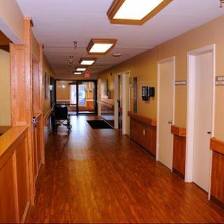 A well-lit hospital hallway with wooden flooring, showcasing doors and a waiting area.