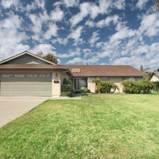 A suburban house with a well-maintained lawn and a clear blue sky dotted with clouds.