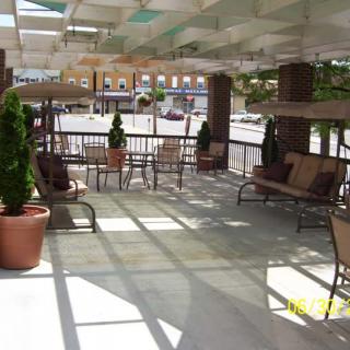 An outdoor patio area with chairs, tables, and potted plants under a partially shaded pergola.