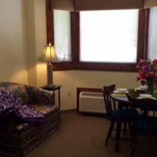 A cozy living room with a sofa, lamp, and a dining table adorned with flowers near the window.
