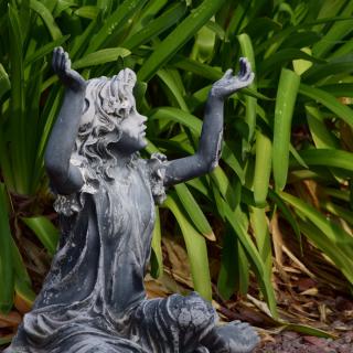 A garden statue of a figure with raised arms surrounded by lush greenery.
