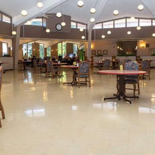 A spacious common area featuring tables and chairs, illuminated by natural light from large windows.