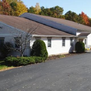 A white building with a paved driveway surrounded by autumn foliage.