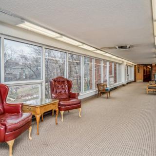 A long hallway with large windows, featuring red leather chairs and a beige carpet.
