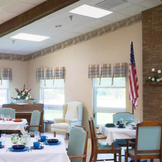 A well-lit dining room with tables set for a meal, featuring an American flag and large windows.