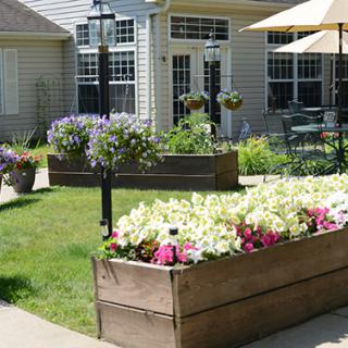 A sunny patio area with raised flower beds filled with colorful blooms, surrounded by a well-maintained garden.