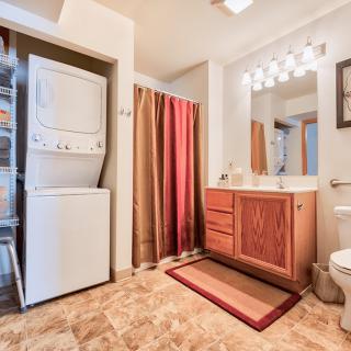 A bathroom with an integrated laundry area, featuring a stacked washer and dryer unit next to a vanity with a large mirror and shower.