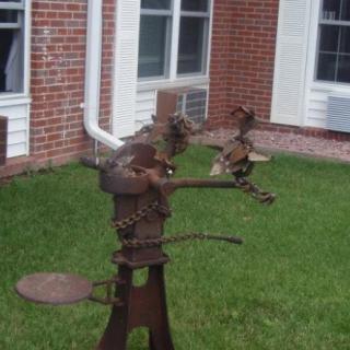 A metal sculpture of birds perched on a banjo in an outdoor garden setting.