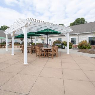 A spacious outdoor patio with tables and chairs under a pergola, featuring umbrellas for shade.