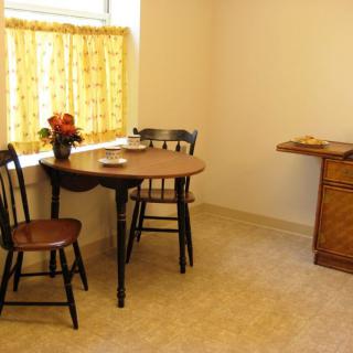 A cozy kitchen corner with a small table, two chairs, and a window with yellow curtains.