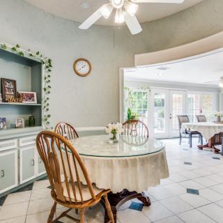 A cozy dining area with a round table and chairs, featuring a ceiling fan and large windows in the background.