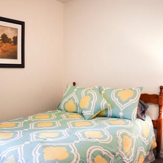 A cozy bedroom with a neatly made bed and colorful bedding, featuring a framed artwork on the wall.