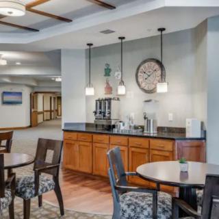 A cozy interior featuring a coffee station with tables and chairs, ambient lighting, and a large wall clock.
