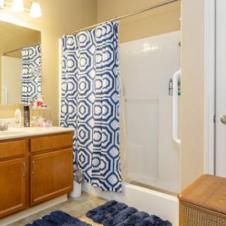 A modern bathroom featuring a blue patterned shower curtain, wooden vanity with mirrors, and coordinated towels.