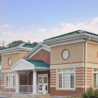 A small brick building with a green roof and multiple windows.