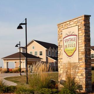 Entrance to a vineyard and winery with a sign and nearby building.