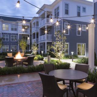 A cozy apartment courtyard with string lights and a firepit at dusk.