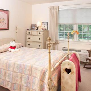 A cozy bedroom with vintage-style decor, featuring a bed, dresser, and rocking chair by the window.