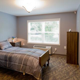 A cozy and well-lit bedroom featuring a single bed, bedside table, and a chest of drawers.