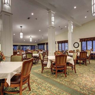A spacious dining room with neatly arranged tables and chairs, featuring elegant lighting and carpeted flooring.