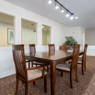 A dining room featuring a wooden table and chairs, with carpeted flooring and overhead lighting.