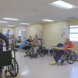 Patients in a nursing home participating in activities, supported by caregivers.
