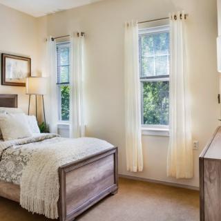 A cozy bedroom with a single bed, light curtains, and natural lighting.