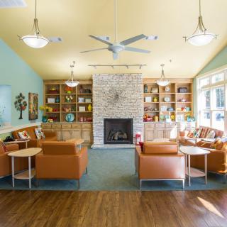 A cozy living room with a central fireplace, surrounded by bookshelves and ample seating, illuminated by natural light.