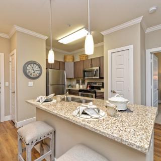 A modern kitchen with granite countertops and stainless steel appliances, featuring pendant lighting and bar stools.