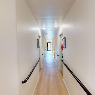 A well-lit hallway featuring doors along the sides and wooden flooring.