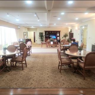 A spacious dining room with several tables and chairs, illuminated by overhead lighting.