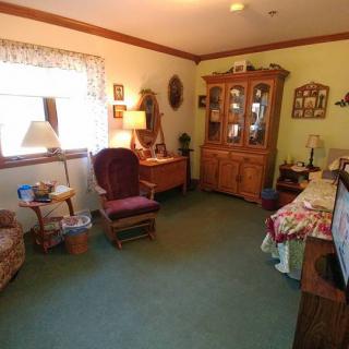 A cozy living room with traditional furniture, including a chair and a wooden cabinet, softly lit by a lamp near the window.