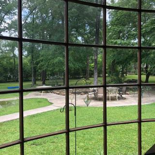 View of a garden through a window with patio furniture and lush greenery.