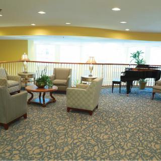 A cozy lounge area with comfortable seating, a grand piano, and natural lighting.